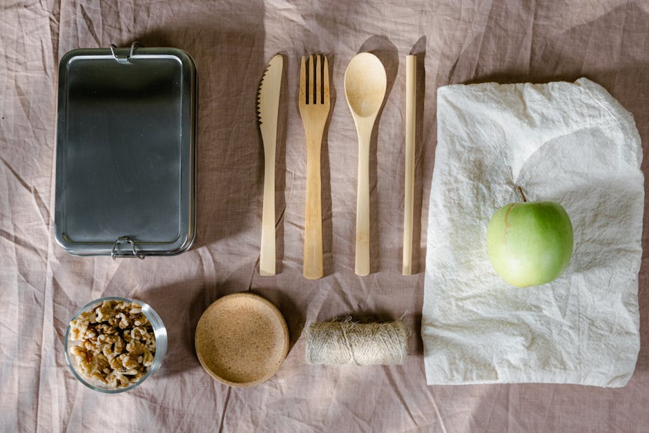 An arranged flat lay of eco-friendly house removal and packing materials on a soft, neutral-colored fabric surface. The image features a rectangular metal container with a hinged lid at the top left,